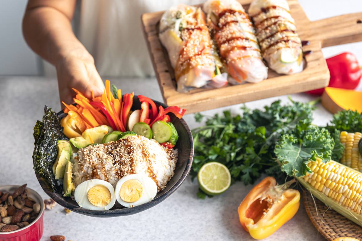 Bowl with vegetables and rice and spring rolls in female hands in the kitchen.