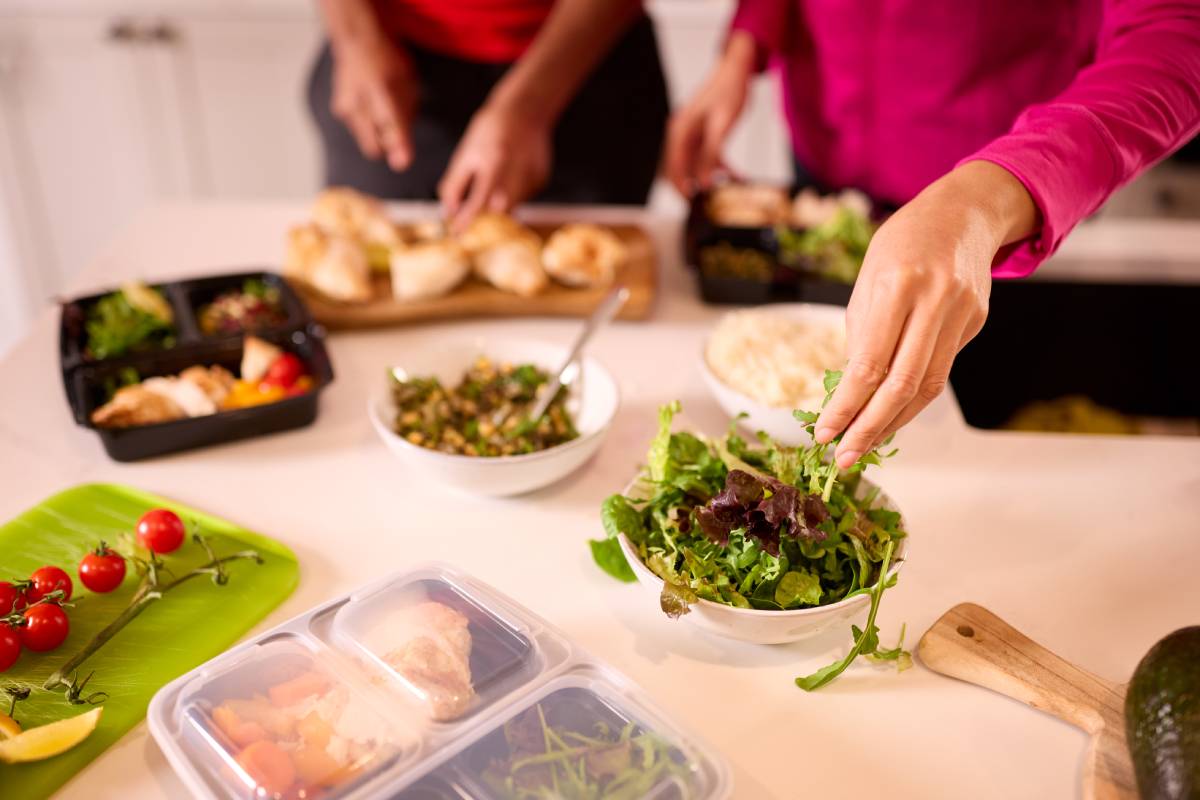 Close Up Of Couple In Kitchen Wearing Fitness Clothing Making Batch Of Healthy Meals For Freezer