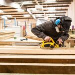 Man wearing ear protectors, protective goggles and dust mask standing in a warehouse, sanding planks of recycled wood. commercial carpentry