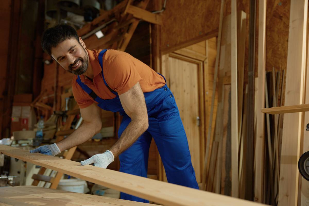 Young man carpenter in uniform putting wood plank on modern equipment