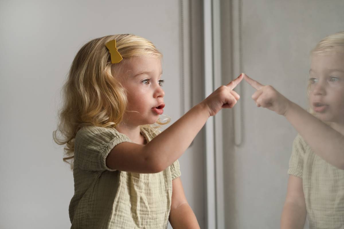 Two year old girl looking through window pointing with her finger somewhere. Half body shot