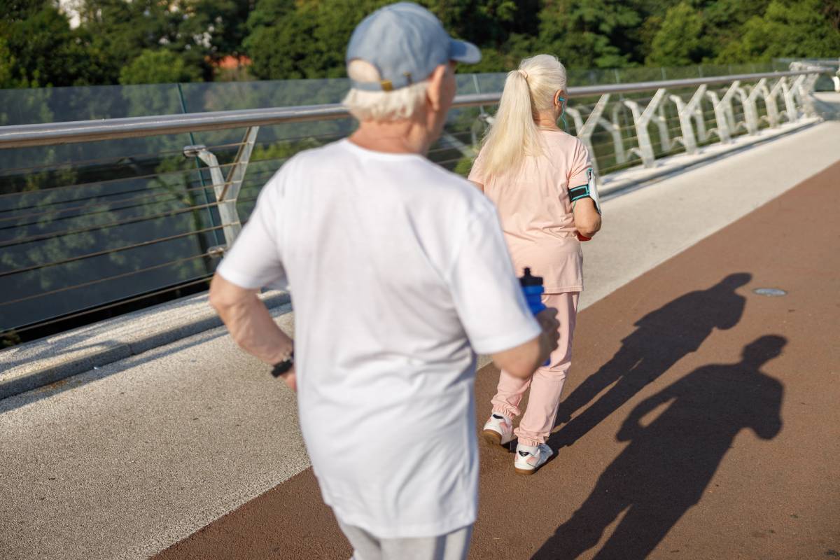 Pair of active pensioners runs together along footbridge on summer day backside view