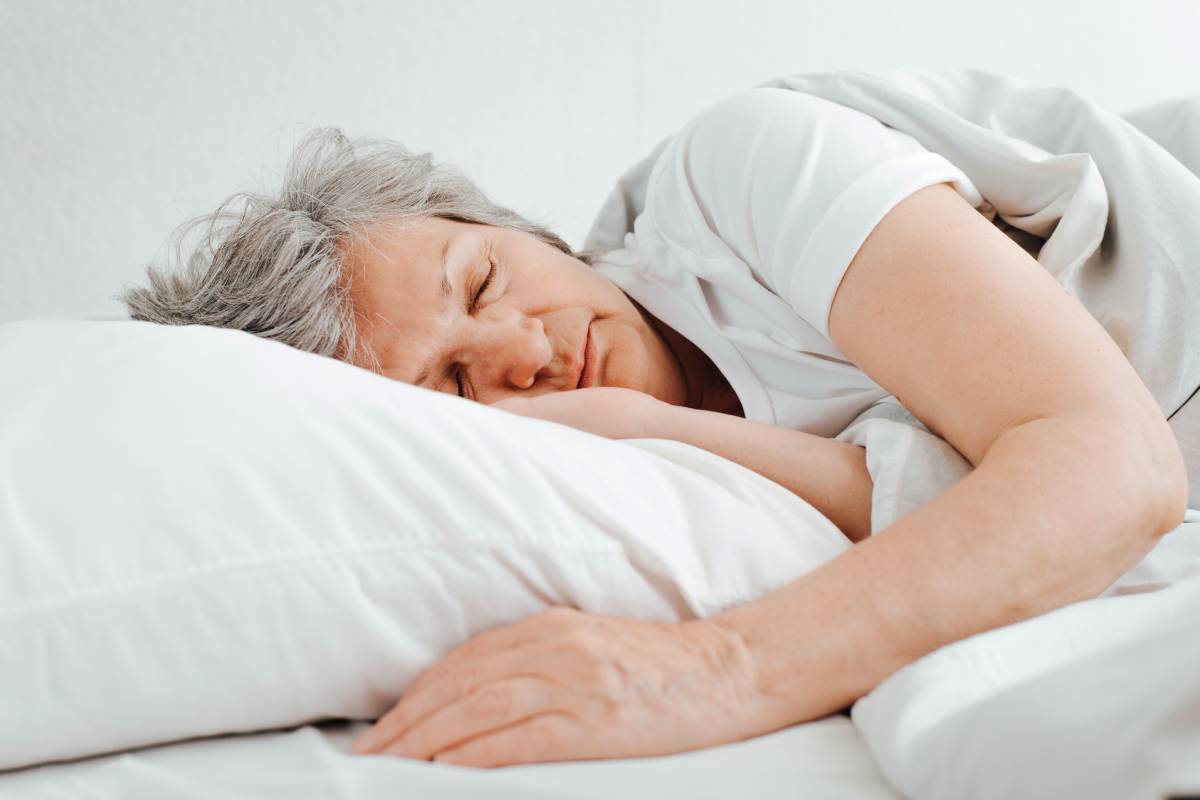 Senior caucasian woman sleeping in comfortable bed, relaxing in bedroom lying on her side. Close-up elderly tired woman morning dream, rest