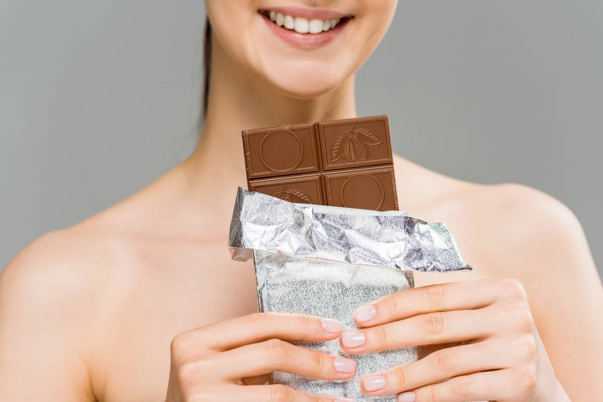 cropped view of smiling young woman holding chocolate bar isolated on grey