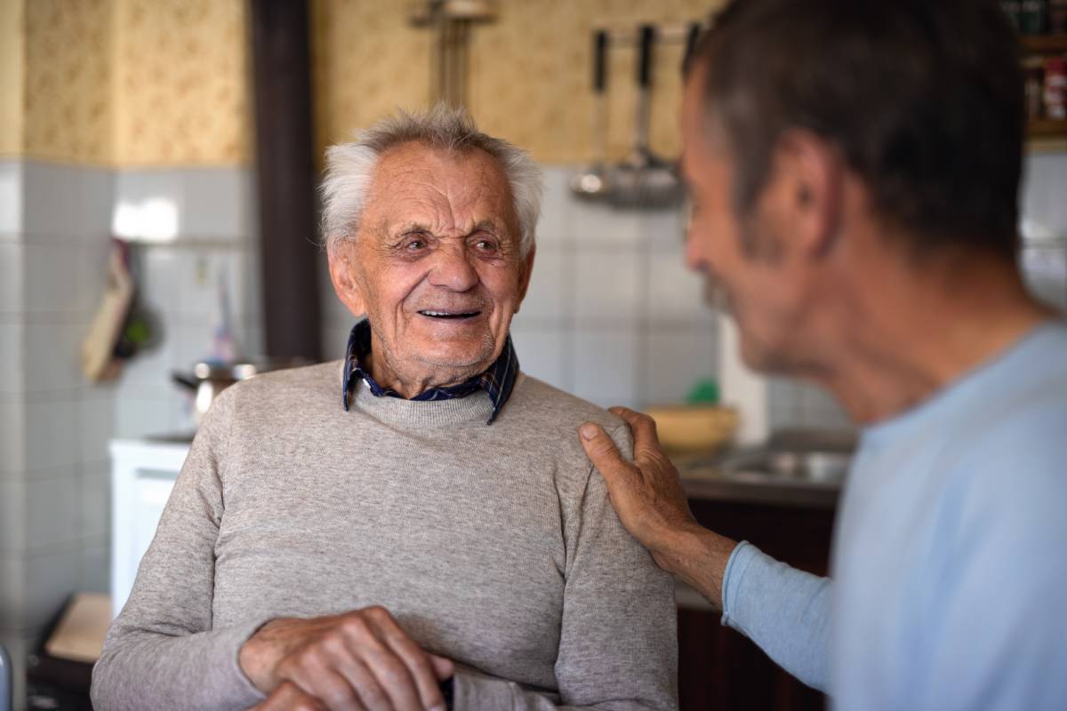 Portrait of man with elderly father sitting at the table indoors at home, talking.