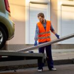 Male road worker in uniform preparing tow truck platform for car loading on city street side